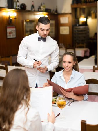Young couple of girls eating out in a restaurant while handsome waiter is serving themの写真素材