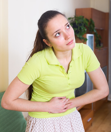 Long-haired woman suffering of disordered stomach holding hands on bellyの写真素材