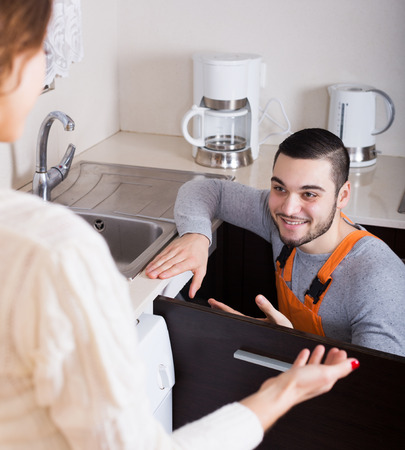 Positive repairman repairing a running water for housewifeの写真素材