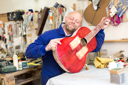 Professional worker at a guitar making manufactory gently hugging a guitar that he's making and smiling with his eyes closedの写真素材