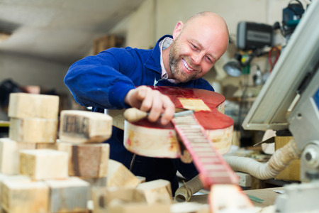Successful smiling adult atelier posing with his guitars at workshopの写真素材