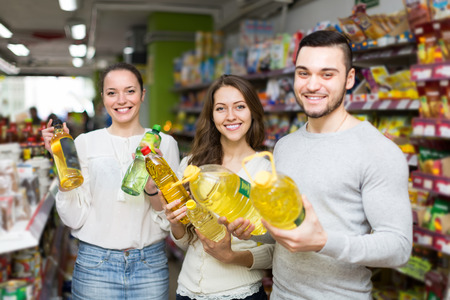 Smiling customers choosing seed-oil in plastic packing at shop. Focus on girlの写真素材