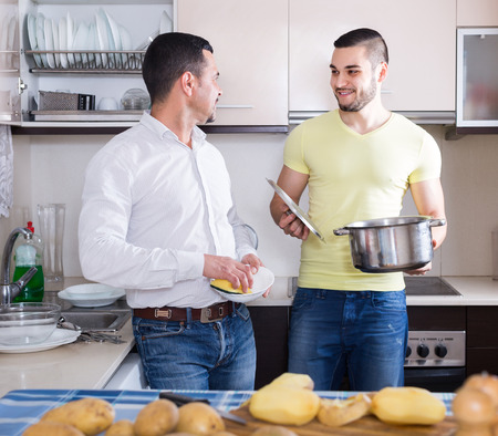 Two cheerful men cooking and doing dishes at home kitchen. Selective focusの写真素材