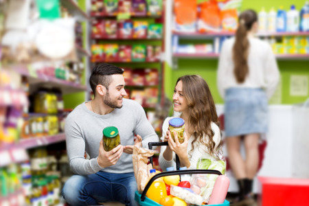 Young smiling couple standing near shelves with canned goods at shopの写真素材