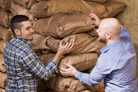 Strong adult workmen unloading shed with coal bagsの写真素材