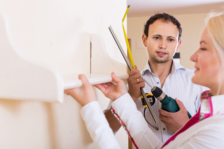 adult couple hangs bookshelf on a wallの写真素材