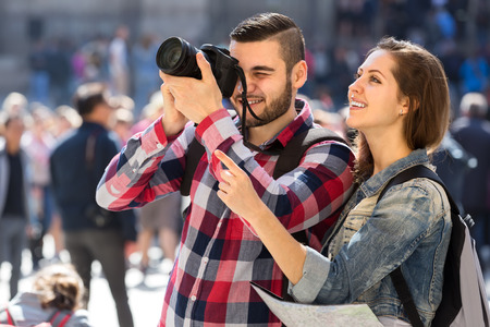 Couple of happy tourists with a map wearing backpacks sightseeing and taking photographsの写真素材