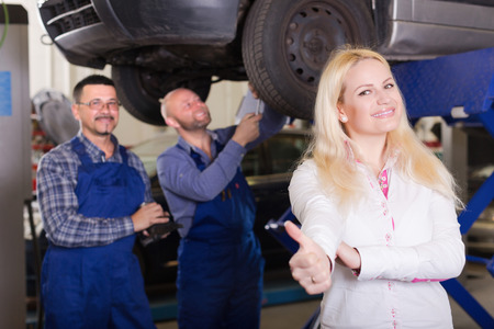 Service crew and happy driver standing near car and smiling indoor. Focus on womanの写真素材