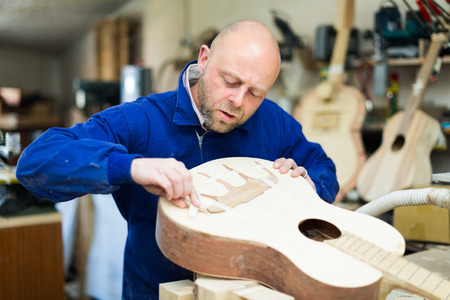 Portrait of professional guitar-maker working with unfinished guitar at workshopの写真素材