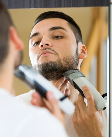 Man looking at mirror and shaving face with electric razorの写真素材