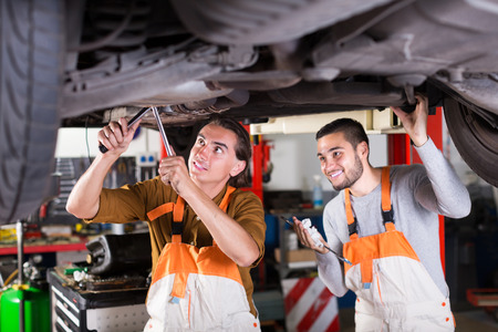 Professional happy young serviceman repairing car of clientの写真素材