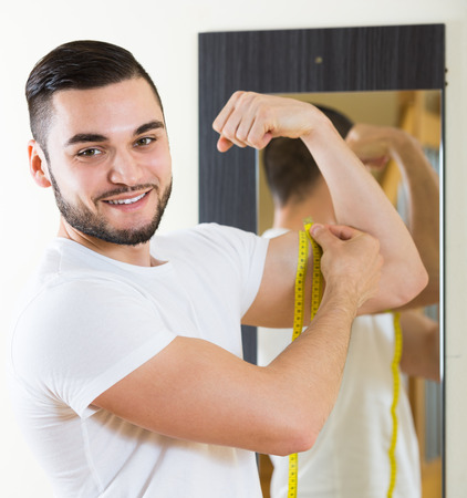 smiling man measuring his bicep and bodyの写真素材
