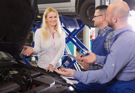 Service crew and happy woman driver standing near car and smiling indoor. Focus on womanの写真素材