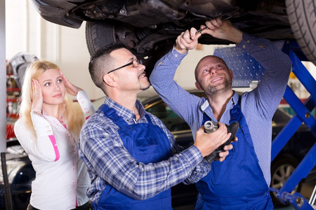 Portrait worried young girl and specialists at auto repair shop. Focus on the right manの写真素材