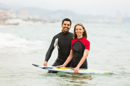 Smiling active couple swimming in wetsuits with surf boardの写真素材