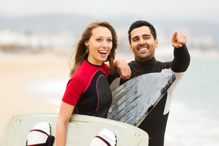 Happy adult couple running on the beach with surf boards. Focus on the womanの写真素材