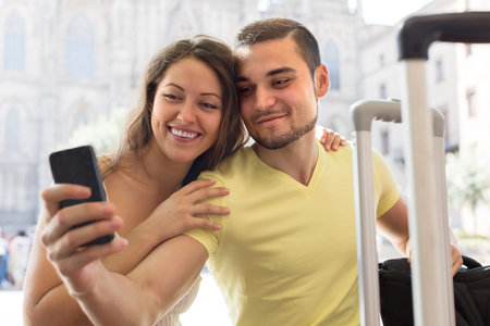 Smiling young couple with luggage doing selfie at travel destination backgroundの写真素材