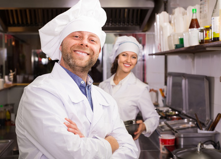 Portrait of hospitable smiling chef and his helper at bistro kitchenの写真素材