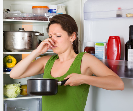 Girl holding her nose because of bad smell from food near refrigerator  at homeの写真素材