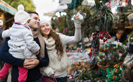 Smiling parents and little child buying red Euphorbia at Christmas fair. Focus on womanの写真素材