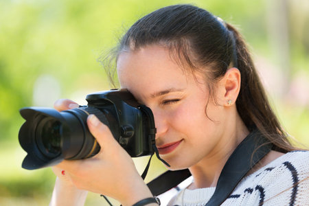 Portrait of young positive girl with photocamera at park
