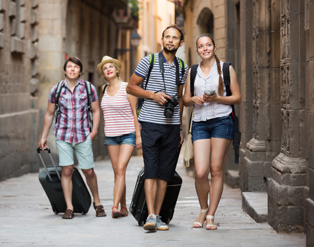 Company of smiling young travelers with travel bags walking the cityの写真素材