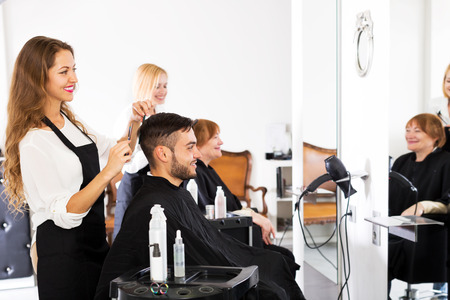 Smiling guy cuts hair and female barber at the hair salonの写真素材