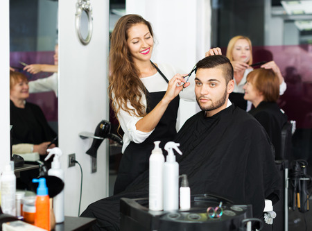 Haircutter makes the cut for young man in the barbershopの写真素材