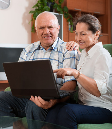 Happy mature couple  with notebook  at table in homeの写真素材