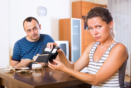 Sad young woman and her husband counting money for paying debtsの写真素材