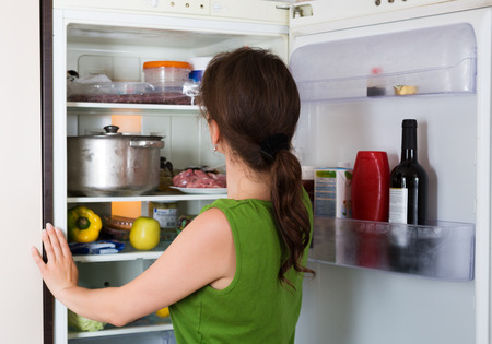 Brunette girl looking for something in fridge at home kitchenの写真素材