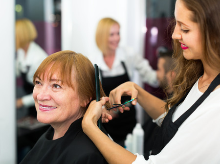 Elderly woman doing haircut at barbershopの写真素材
