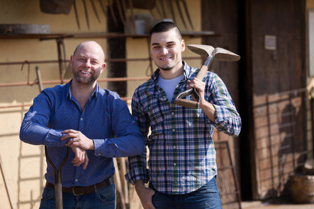 Two smiling male farmers standing with spades at farmyardの写真素材