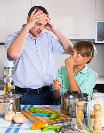 Stressed middle age man and son cooking together at kitchenの写真素材