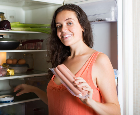 Young girl taking sausages from refrigerator  at homeの写真素材