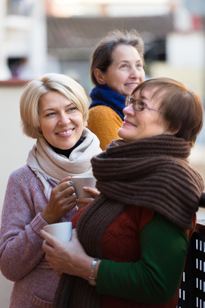 Portrait of cheerful female pensioners drinking coffee at patio. Focus on blondeの写真素材
