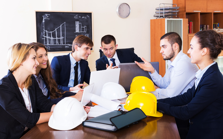 Portrait of professionals with helmets and laptops having meeting indoors. Focus on the right manの写真素材