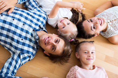 Smiling parents with two little daughters relaxing at homeの写真素材