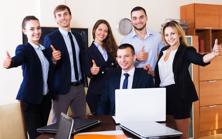 Prosperous business team smiling and posing in office. Focus on sitting man