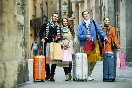 Two smiling couples of tourists with shopping bags and luggage on city streetの写真素材