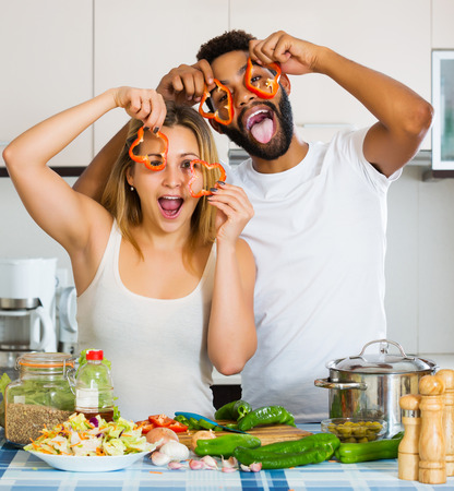 Portrait of happy interracial couple cooking vegetables and laughingの写真素材