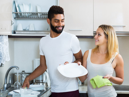 black man with smiling white woman dusting in domestic kitchenの写真素材