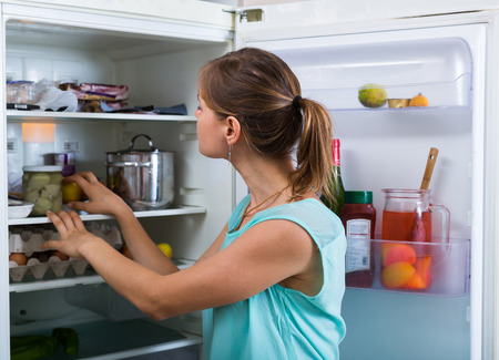 Young woman standing near refrigerator filled with productsの写真素材