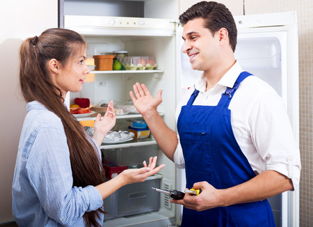 Young  housewife and cheerful handyman with tooling standing near fridge indoorsの写真素材