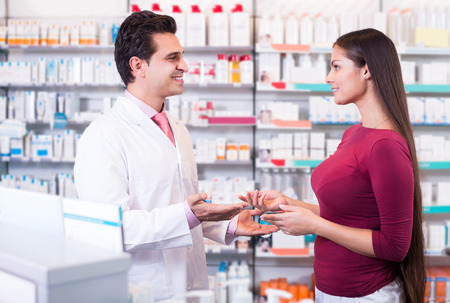 Professional pharmaceutist in drugstore helping girl to choose medicationの写真素材