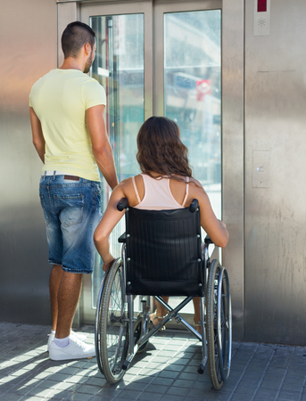 Handsome man helping handicapped girlfriend at outdoor elevatorの写真素材