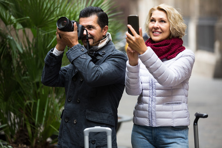 american mature couple walking with luggage, camera and smartphoneの写真素材