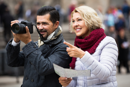 Aged happy spanish tourists with map and luggage on city streetの写真素材
