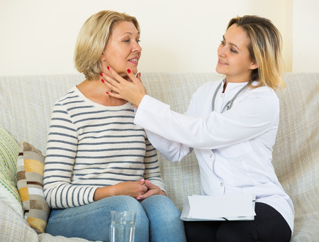 Mature woman with sore throat receiving doctor at homeの写真素材
