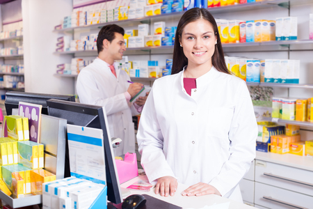 Cheerful pharmacist standing at pay desk and pharmacy technician helpingの写真素材